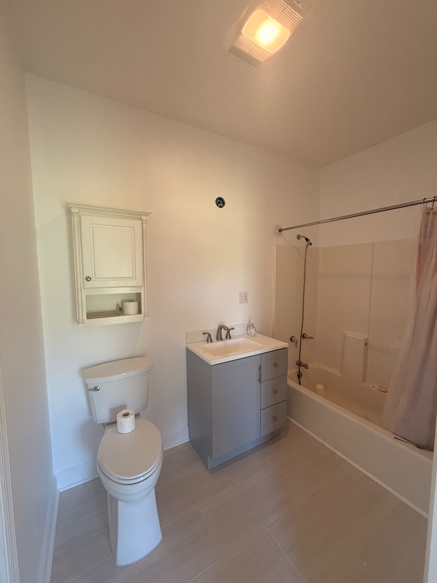 Completed bathroom remodel with gray vanity, tile floor and new tub and shower surround