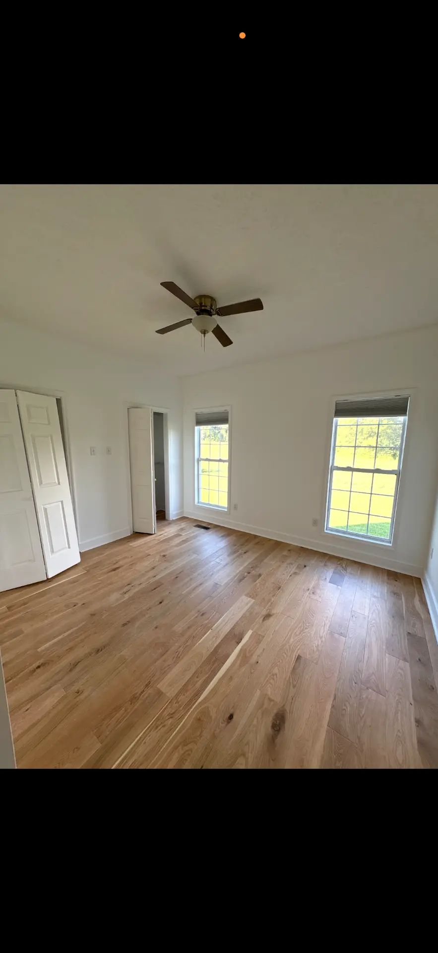 Remodeled bedroom with new white oak hardwood flooring, fresh white walls and a ceiling fan